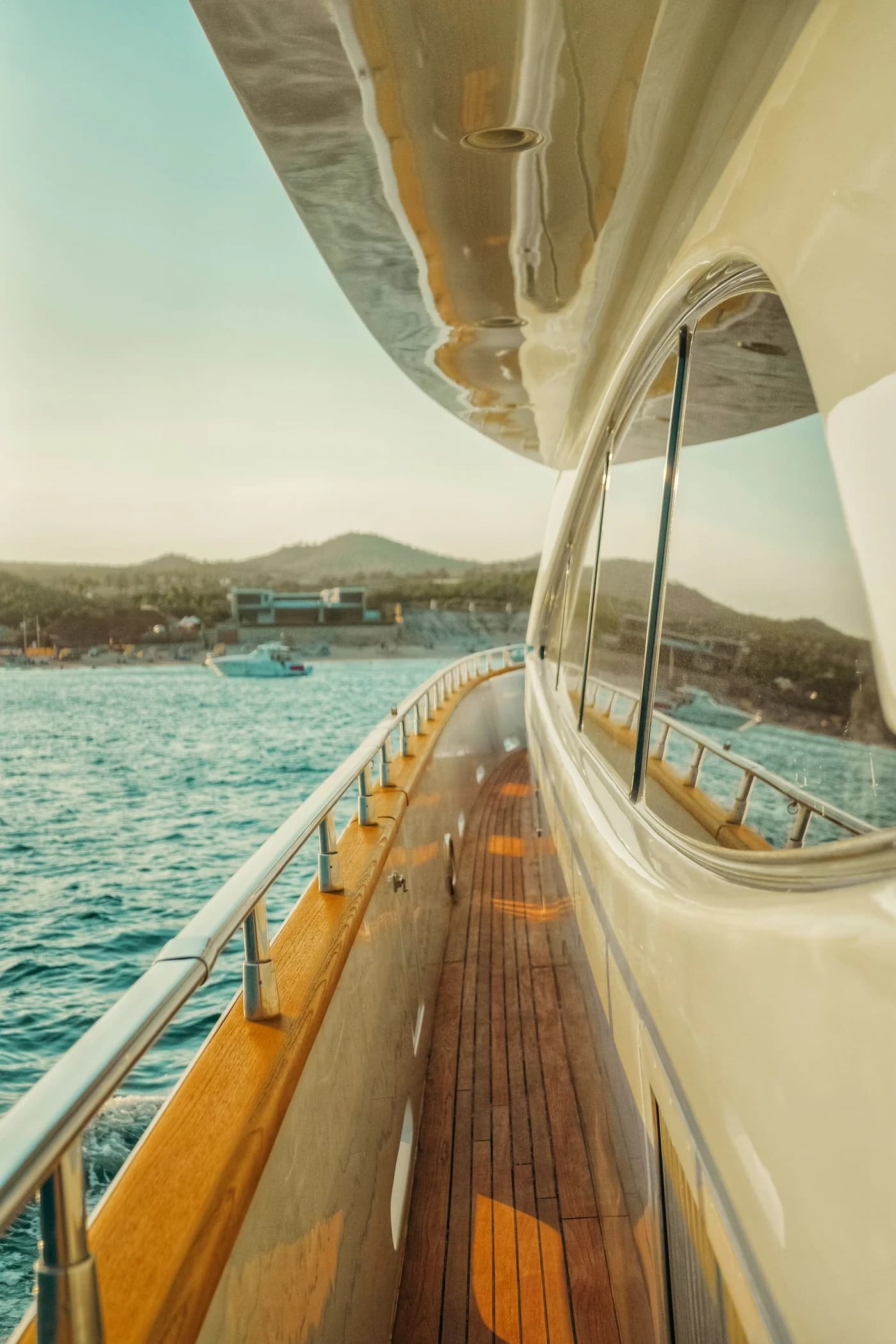 Sunlit teak yacht deck overlooking the sea and a green coastline